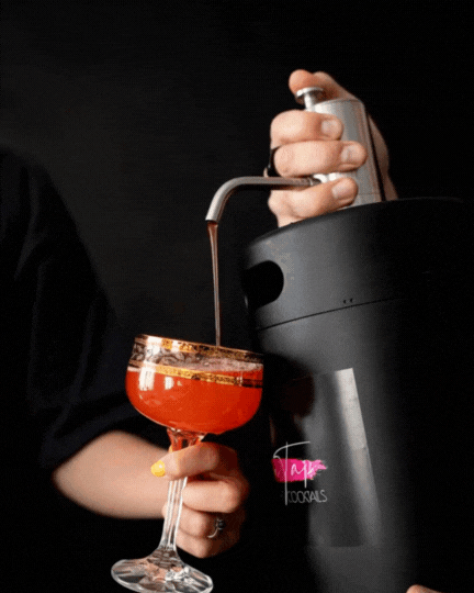 Rankose laikoma kokteilių statinė su pilamu kokteiliu į taurę.